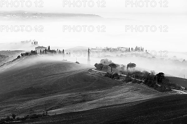 Country houses on hilly landscape in morning mist, black and white shot