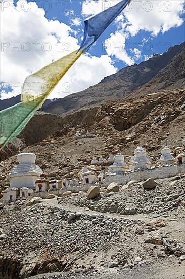 Small white stupa on the mountainside, prayer flags in front