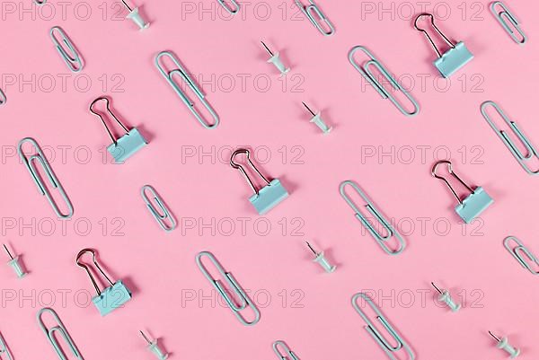 Stationery items like paper clips and drawing pins arranged on pink background,