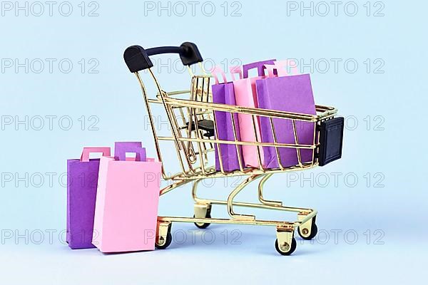 Golden shopping cart filled with pink and purple paper shopping bags on blue background,