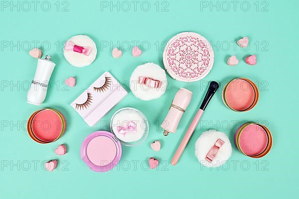 Cute pink makeup beauty products like brushes, powder or lipstick on teal blue background