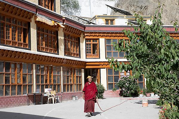 Monk with garden hose in the monastery courtyard, Buddhist Yellow Cap Monastery Rizong or Rhizong or Yuma Changchubling