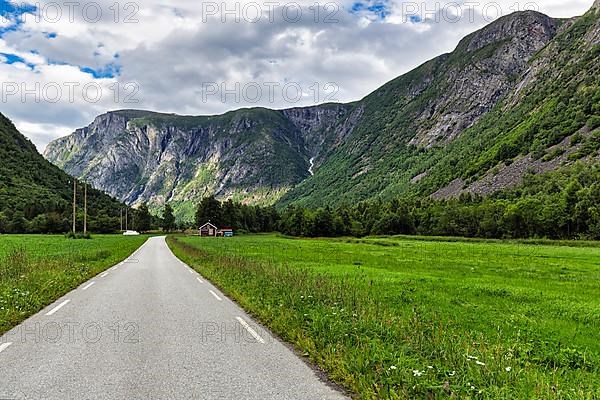 Single-lane country road through valley, typical landscape with high mountains