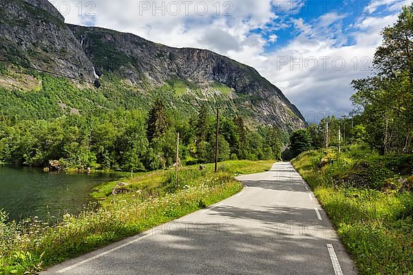 Single-lane country road through valley, river Aura