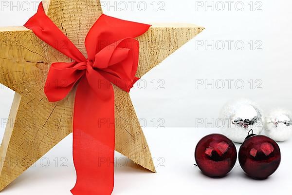 Christmas wooden star with a red bow on a white background, silver and red Christmas tree balls on the side