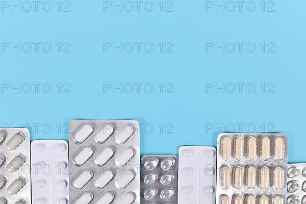 Blister packs with various pills and capsules at bottom of blue background with copy space,