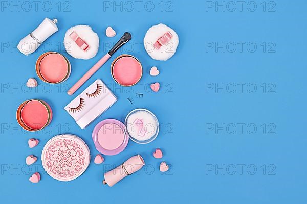 Pink makeup beauty products like brushes, powder or lipstick on side of blue background with empty copy space