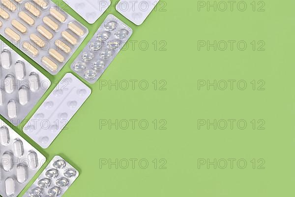 Different capsules and pills in blister packs on right side of green background with copy space,