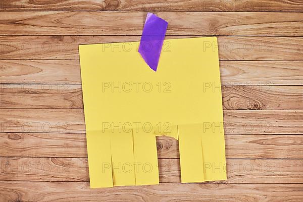 Yellow empty tear-off stub paper note without text on wooden wall,