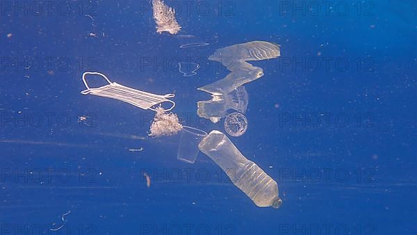 Plastic bottle, cups and medical face mask swim in the blue water. Discarded plastic and other debris slowly drifting under surface of blue water in sunlight. Plastic pollution of the Ocean. Red sea