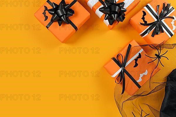 Traditional decorated gift boxes for Halloween with small bats and mesh with spiders on yellow background with empty copy space,