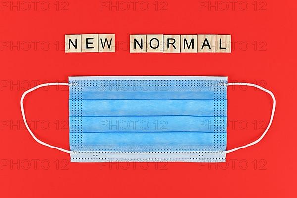 Flat lay with blue disposable protective face mask and wooden letters forming words new normal on red background,
