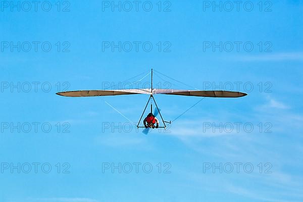 Motorised hang glider flying in slightly cloudy sky, text free space