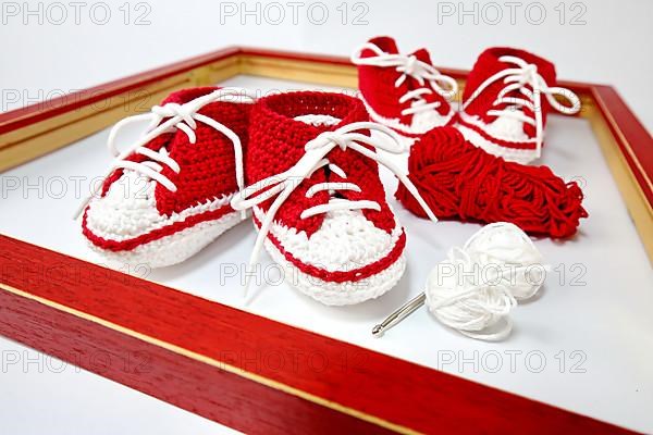 Baby shoes or crochet shoes in red and white isolated against a white background,