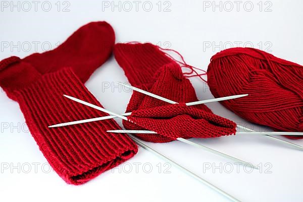 Self-knitted red socks made of wool isolated against a white background with knitting needle and ball of wool,