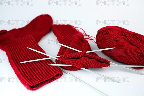 Self-knitted red socks made of wool isolated against a white background with knitting needle and ball of wool,