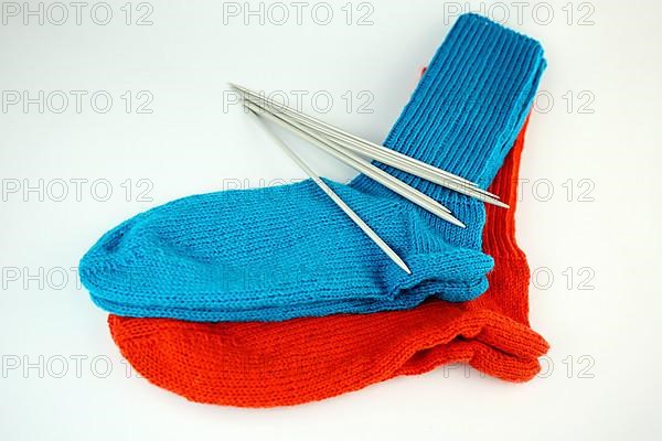 Self-knitted socks made of wool isolated against a white background in orange and blue with knitting needle and ball of wool,