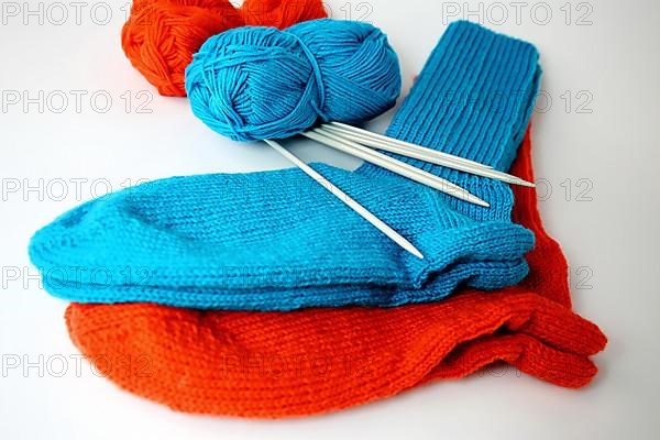 Self-knitted socks made of wool isolated against a white background in orange and blue with knitting needle and ball of wool,