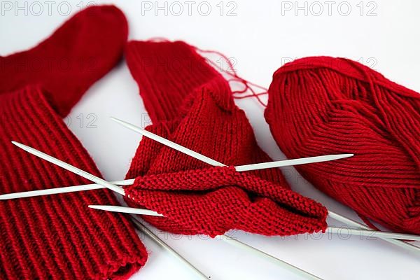 Self-knitted red socks made of wool isolated against a white background with knitting needle and ball of wool,