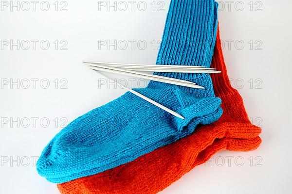 Self-knitted socks made of wool isolated against a white background in orange and blue with knitting needle and ball of wool,