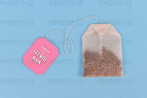 Tea bag with made up cute pink label with text Get well soon on pastel blue background,