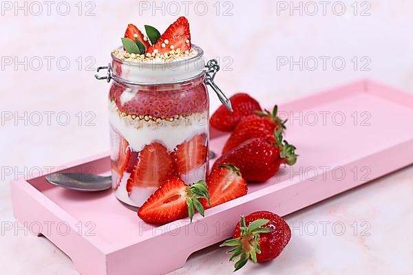 Strawberry fruit dessert with yogurt, healthy chia seeds and puffed quinoa grains layered in jar surrounded by berries on pink wooden tray