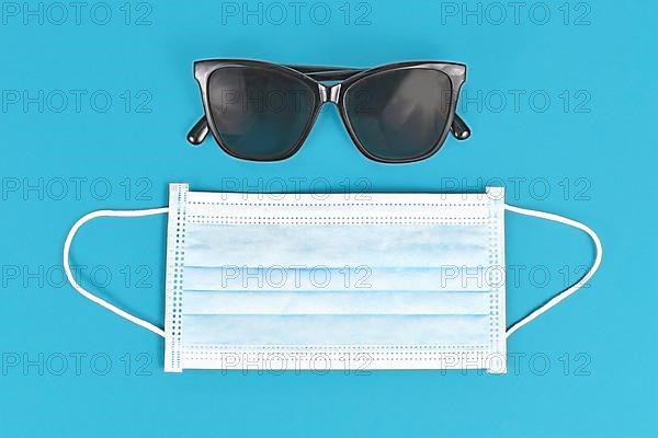 Concept for Summer during Coronavirus crisis with face mask and sunglasses on blue background,