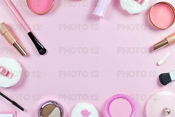 Flat lay with various makeup beauty products like brushes, powder or lipstick surrounding pastel pink background with empty copy space