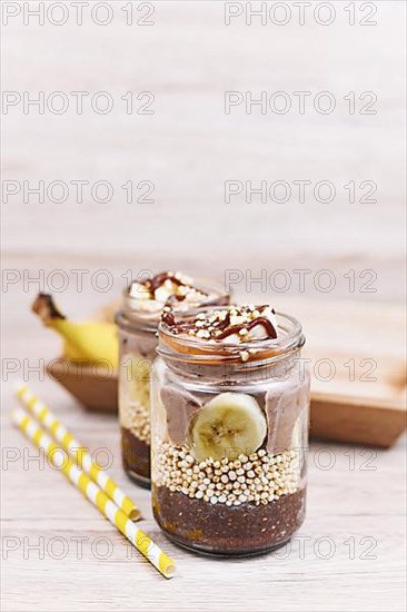 Layered healthy dessert with banana fruit slices, puffed quinoa grain and chocolate chia seed pudding in jar