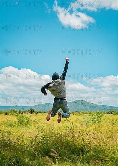 Rear view of man jumping in the grass raising fist, Concept of a free person jumping and raising his arm