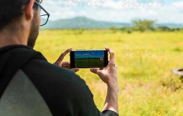 Close up of man hands taking photos of a landscape with the cell phone. Rear view of a person taking a photo of a field with his cell phone, rear view of a man taking photos of a field