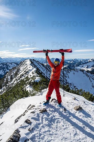Ski tourer lifts his skis into the air at the summit of Jagerkamp, winter