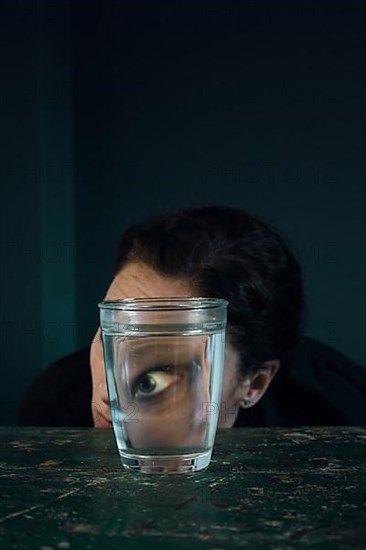 Face of a woman, eye reflected in a water glass