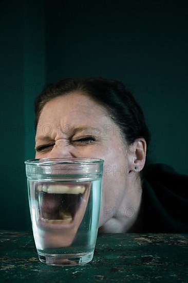 Angry face of a woman reflected in a glass of water,