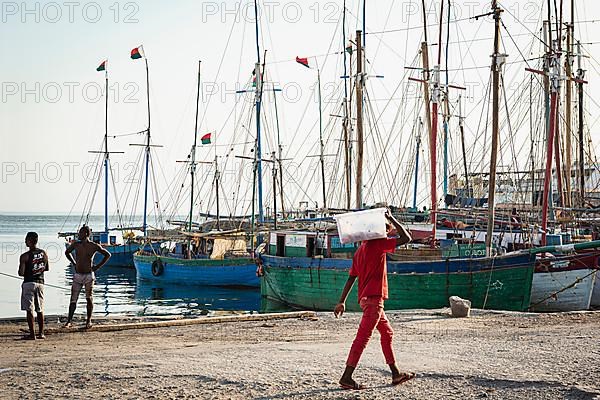 Man in red clothes carrying sack, fishing boats behind