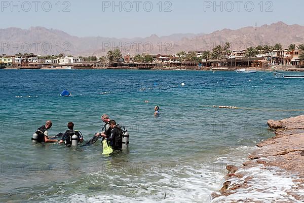 Divers walk into Red Sea water from shore in Dahab prepare for dive, Dahab