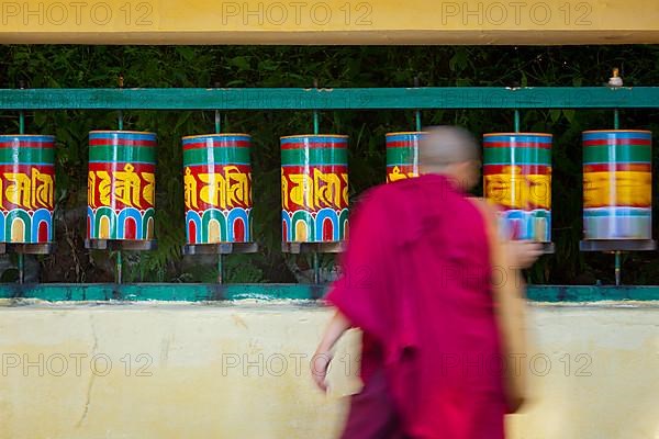 Buddhist monk passing and rotating prayer wheels on kora around Tsuglagkhang complex in McLeod Ganj