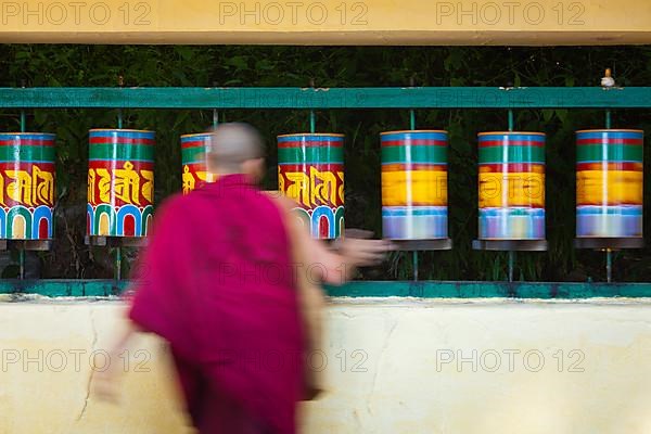 Buddhist monk passing and rotating prayer wheels on kora around Tsuglagkhang complex in McLeod Ganj