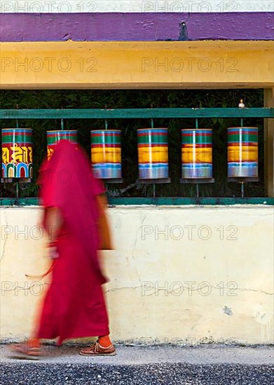 Buddhist monk with prayer beads passing and rotating prayer wheels on kora around Tsuglagkhang complex in McLeod Ganj