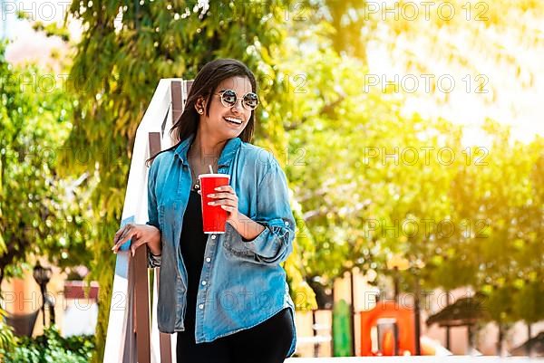 Concept of a smiling woman holding her drink on a sunny day