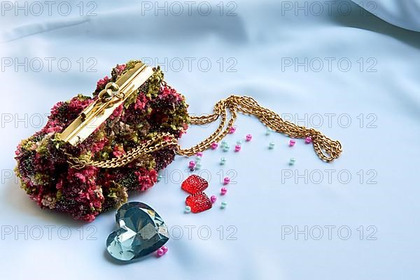 Hand-sewn handbag with a gold chain on a white background with folds