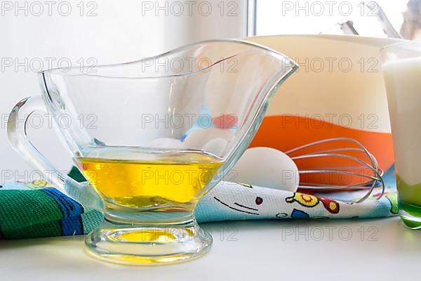 Sunflower oil in a glass transparent oiler on a white windowsill next to the ingredients for pancakes
