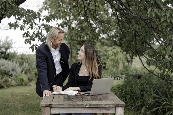 Businessman and businesswoman working in the open on a laptop at a wooden table