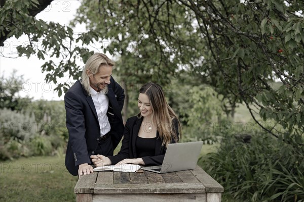 Businessman and businesswoman working in the open on a laptop at a wooden table