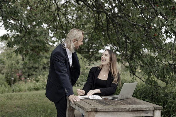 Businessman and businesswoman working in the open on a laptop at a wooden table