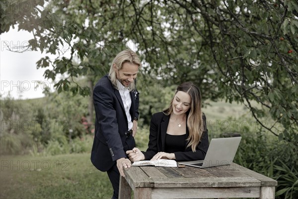 Businessman and businesswoman working in the open on a laptop at a wooden table