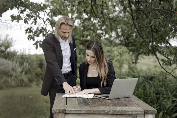 Businessman and businesswoman working in the open on a laptop at a wooden table