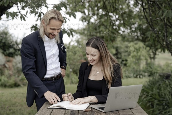 Businessman and businesswoman working in the open on a laptop at a wooden table