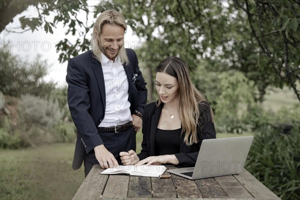 Businessman and businesswoman working in the open on a laptop at a wooden table