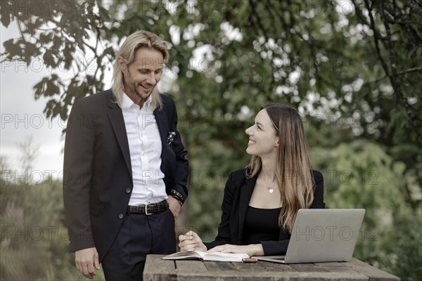 Businessman and businesswoman working in the open on a laptop at a wooden table